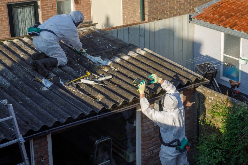Certified asbestos abatement crew removing hazardous corrugated sheeting from a garage roof