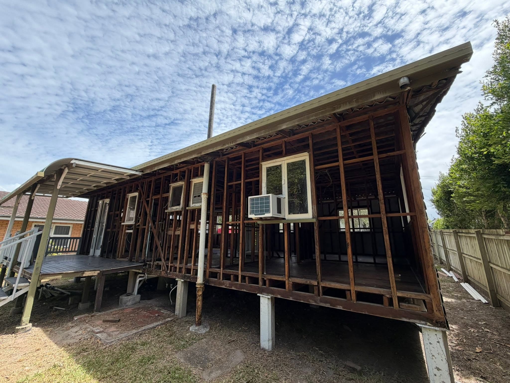 Exposed wooden framing of a house under renovation, elevated on stilts with an open lower level and blue sky above