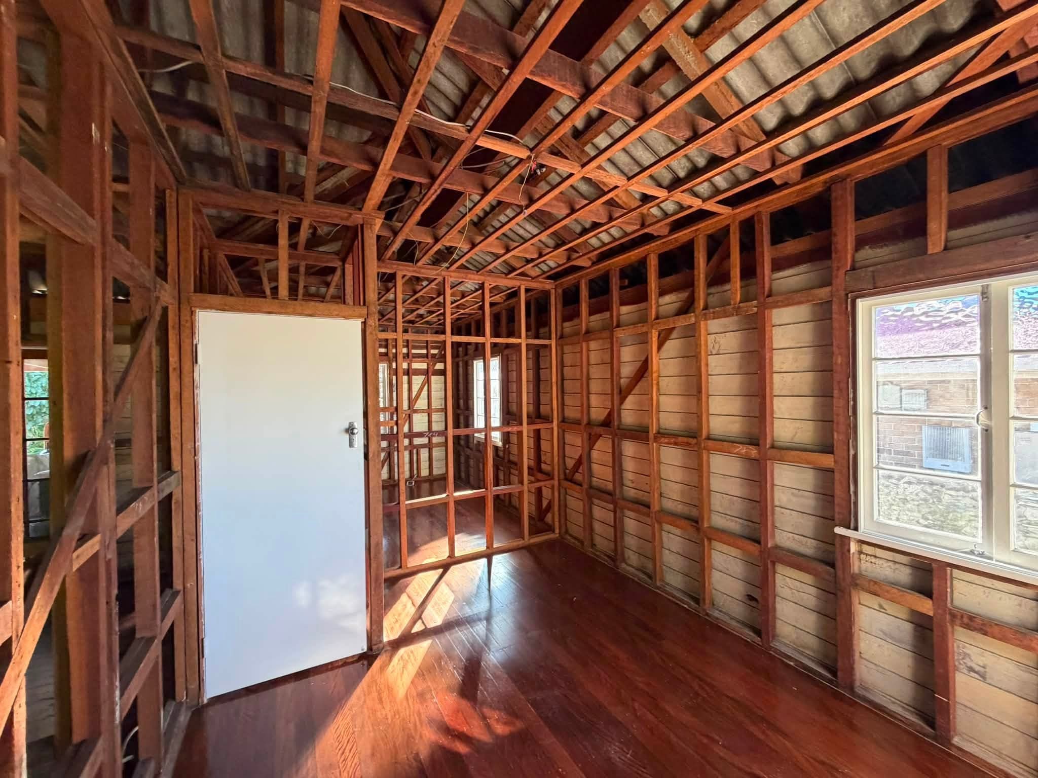 Unfinished interior with exposed wooden studs, rafters, and a white door in a partially built room.