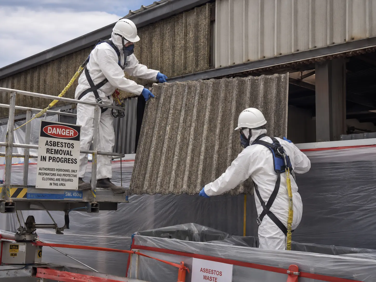 Licensed asbestos removal workers removing corrugated asbestos wall sheeting from an industrial building in Brisbane