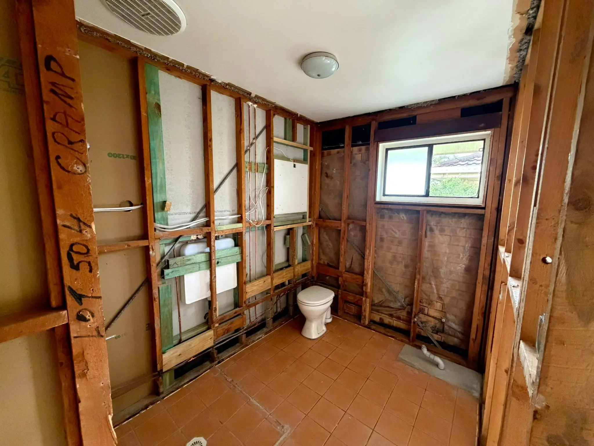 Bathroom under renovation with exposed studs, plumbing, and a white toilet near a window.