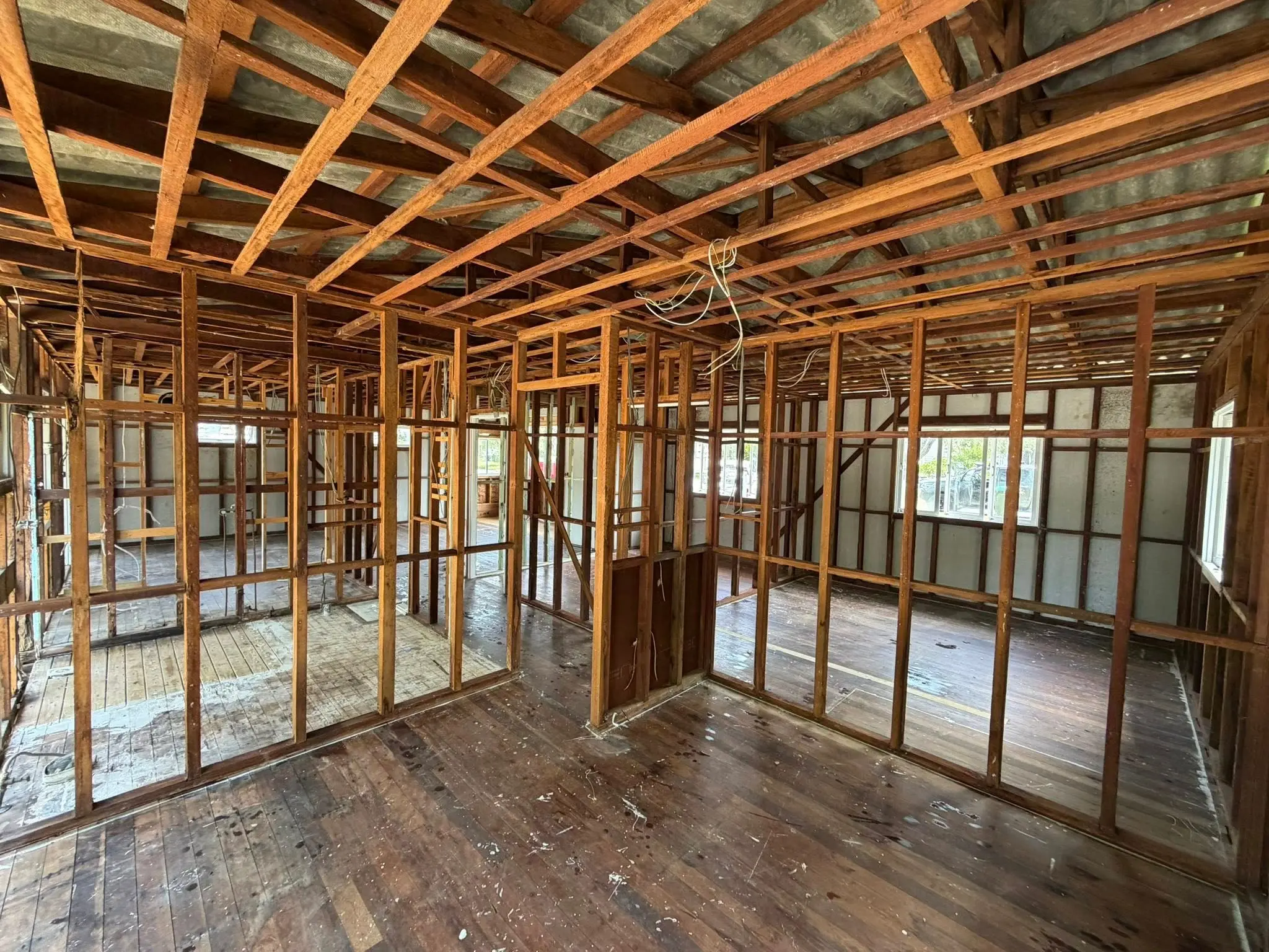 Interior of a partially finished room under renovation with exposed wooden studs and ceiling joists and loose wiring hanging down.