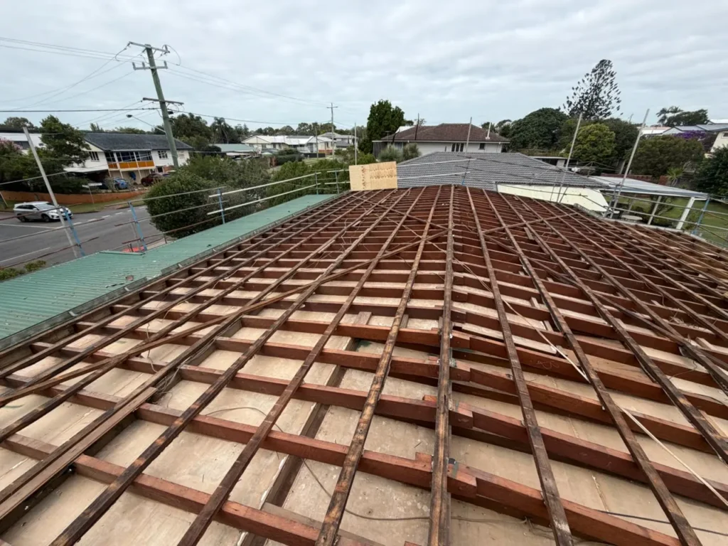 Perspective view of a roof under renovation with evenly spaced brown wooden battens over plywood, scaffolding along the edge, in a residential neighborhood.
